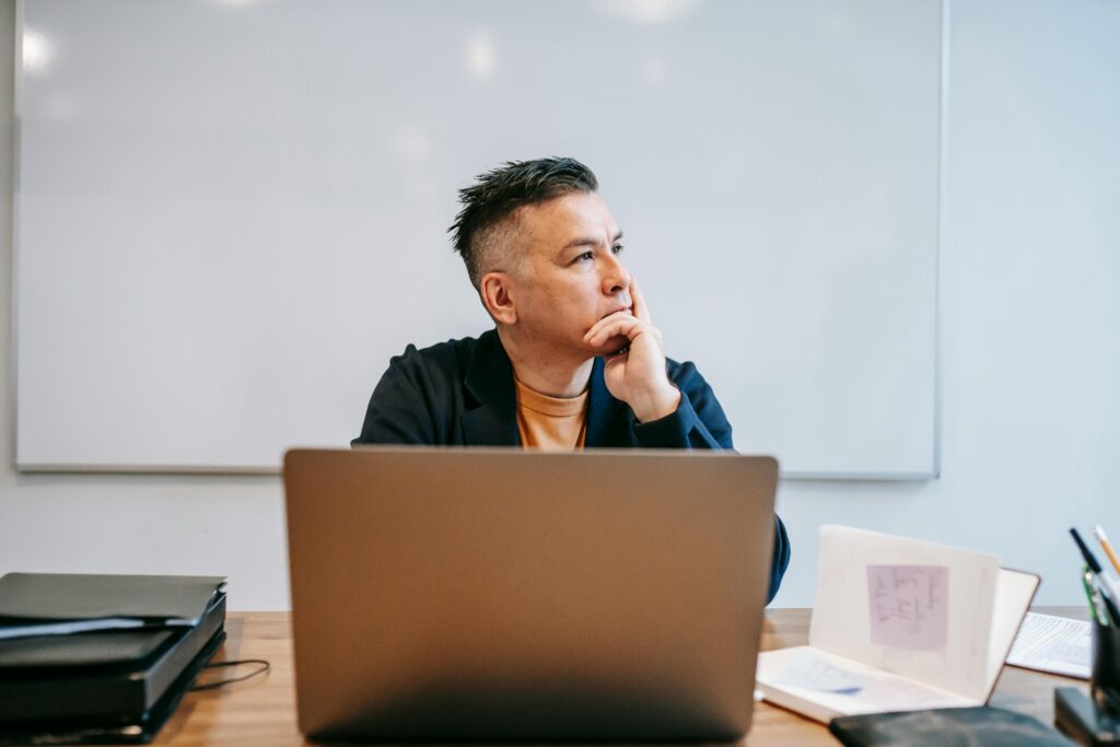 Thoughtful man looking away while working at a laptop in a modern office